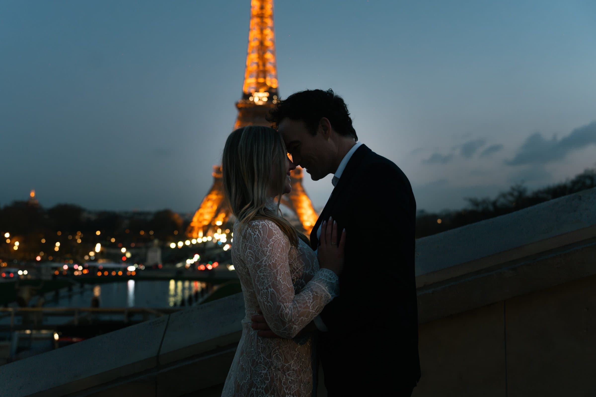 A couple forehead to forehead at Trocadéro, the Eiffel Tower lit behind them at blue hour